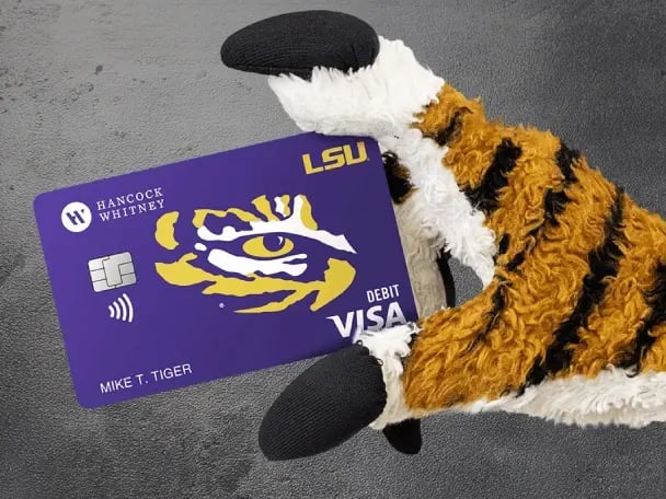 Mike the Tiger's hand holding an LSU debit card from Hancock Whitney
