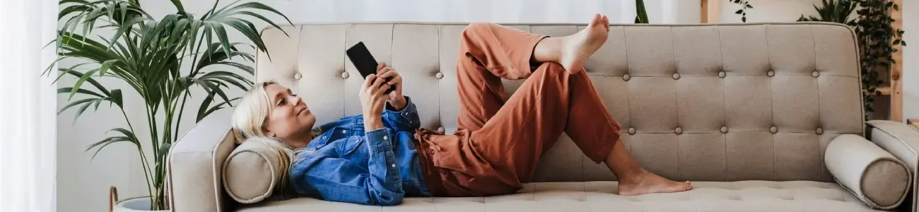 Woman using digital banking on her mobile phone while relaxing on a couch